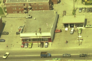 Eine Luftaufnahme einer Stadt mit zahlreichen Autos, die um Gebäude herum geparkt sind und einige Autos auf der Straße fahren.