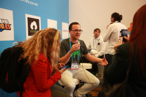 Ein Interview findet mit Menschen mit Mikrofonen und einer Kamera statt, mit Personen im Vordergrund und einem Banner links, während der Hintergrund klar ist.