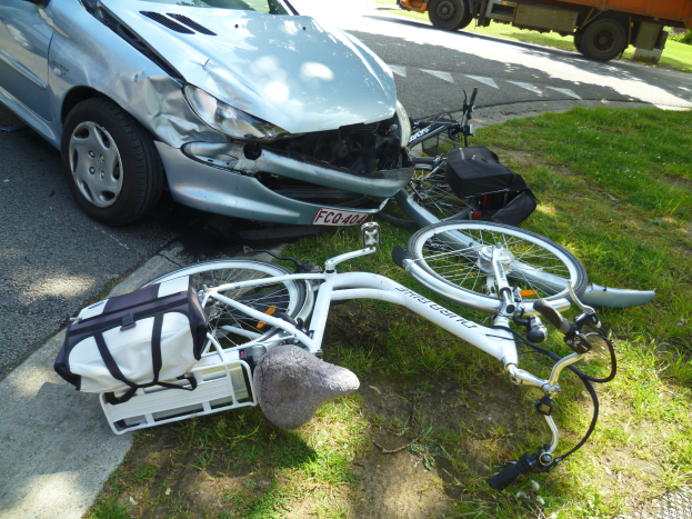 Auto am Straßenrand mit einem Fahrrad in der Nähe auf dem Gras, Bäume und klarer blauer Himmel im Hintergrund.