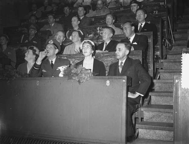 Schwarzes und weißes Foto einer Menge, die in einem Stadion auf einem Podium mit einem Blumenstrauß sitzt, Treppen auf der rechten Seite sichtbar