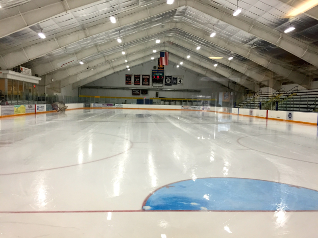 Großes Hallen-Eisstadion mit Deckenbeleuchtung, Werbetafeln, einer Wand, Treppen mit Geländern und einigen Menschen, was auf eine Sportanlage hinweist, die likely für Hockey verwendet wird.