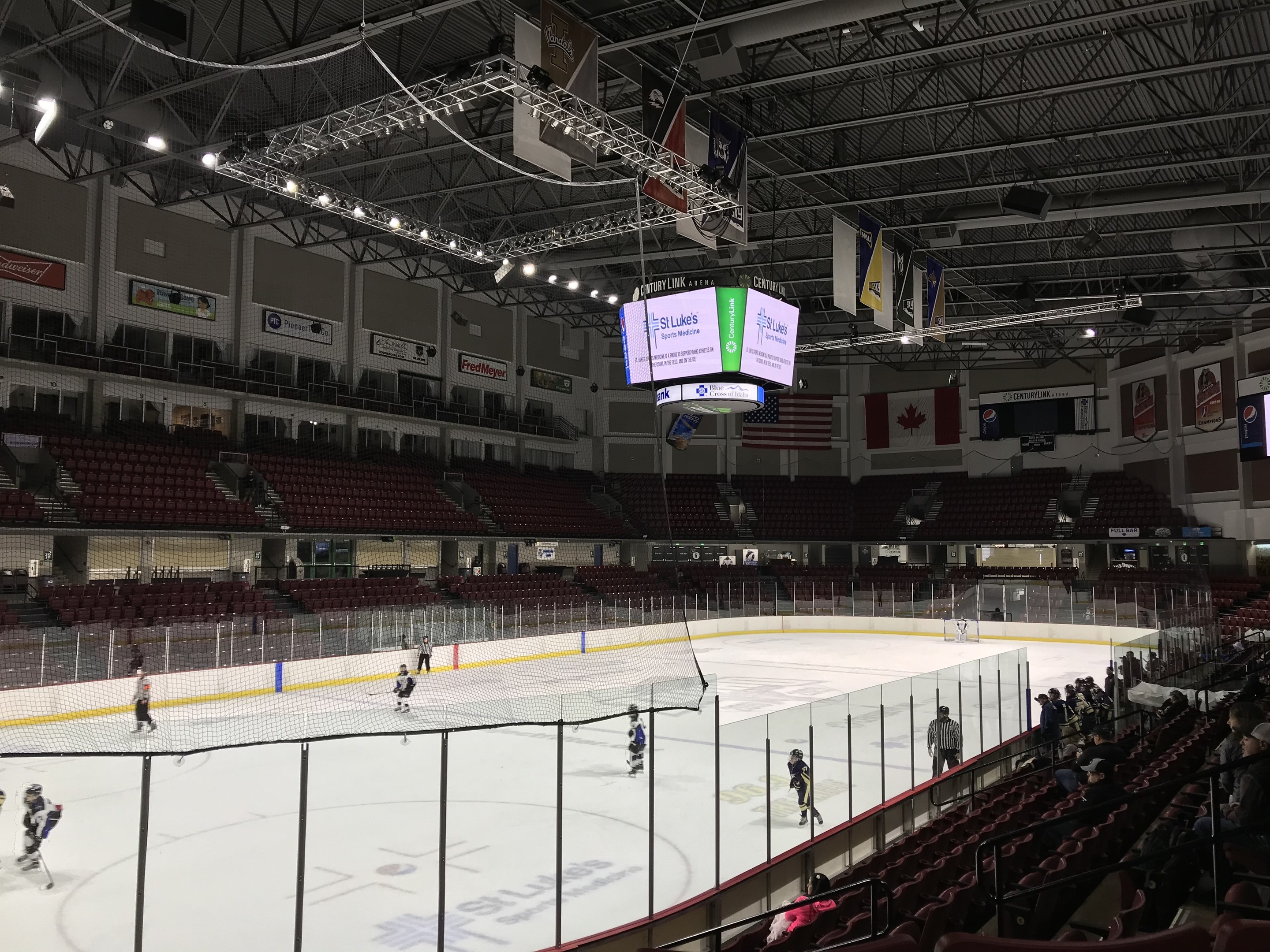 Eishockeyspiel in einer großen Arena mit einem zentralen Netz, Zuschauern auf Stühlen, Deckenbeleuchtung und Trägern, Bannern und Fahnen; die Arena ist als St. Louis Blues Arena identifiziert.
