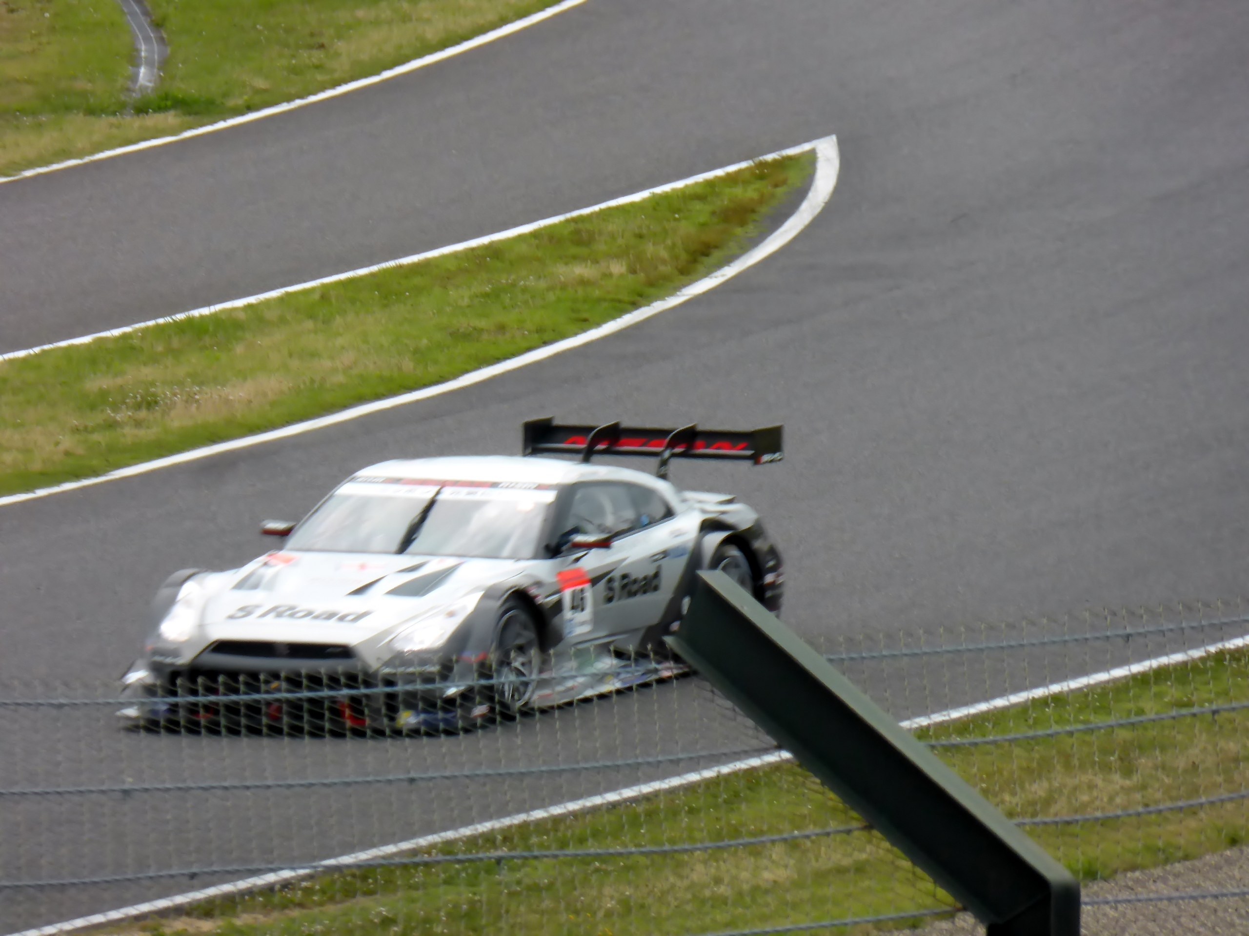 Audi R8 LMS GT3 auf der Nürburgring 24 Stunden Rennstrecke, umgeben von einem Metallzaun und grünem Gras, mit der Strecke, die sich vor ihr erstreckt.
