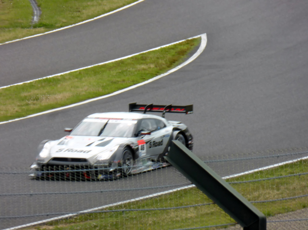 Audi R8 LMS GT3 auf der Nürburgring 24 Stunden Rennstrecke, umgeben von einem Metallzaun und grünem Gras, mit der Strecke, die sich vor ihr erstreckt.
