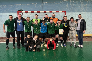 Eine Gruppe von Männern in Medaillen, einer hält einen Pokal, steht auf einem Futsal-Platz mit einem Tor und einer Wand im Hintergrund, feiert ihren Futsal-Weltmeister-Titel.