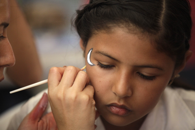 Ein Make-up-Artist trägt Make-up mit einem Pinsel auf das Gesicht eines jungen Mädchens auf, während der Hintergrund unscharf ist.