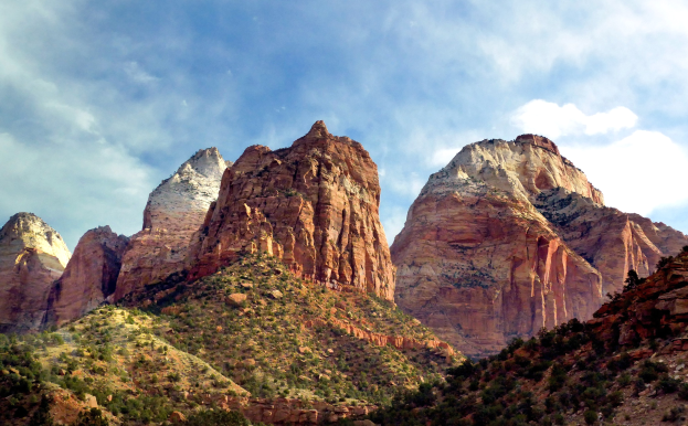 Ein malerischer Blick auf den Zion-Nationalpark in Utah mit majestätischen Bergen, grünen Bäumen, steinigem Gelände und einem Himmel mit weißen Wolken.