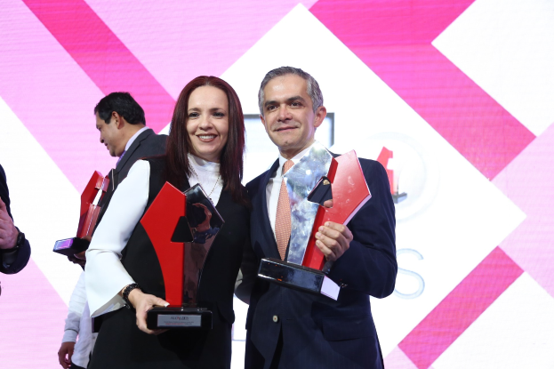 Zwei Menschen, die strahlend auf einer Bühne stehen und Trophäen halten.