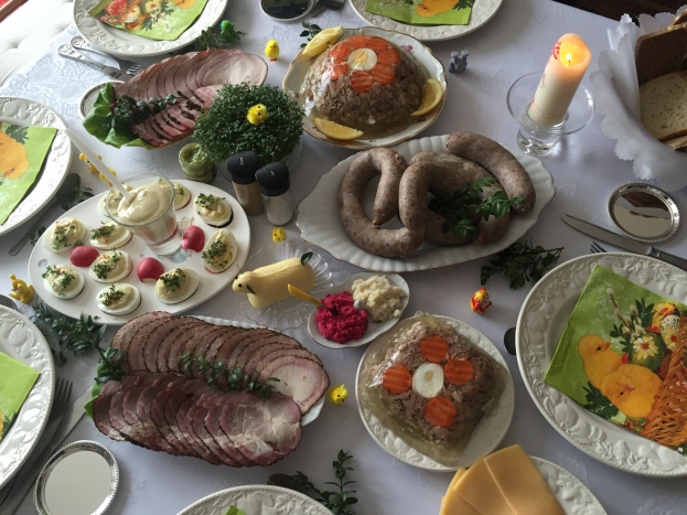 Ein lang gedeckter Tisch mit verschiedenen Gerichten, Besteck, Gläsern und Kerzen, umgeben von Stühlen, was auf ein traditionelles deutsches Osteressen hinweist.