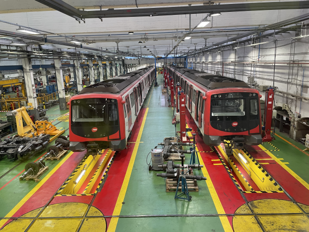 Zwei Züge auf Schienen innerhalb einer Daimler Group-Fabrik mit Maschinen und Rohren an der rechten Wand.