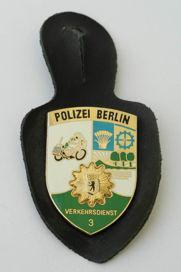 Ein schildförmiges Polizeibadgebnis mit "Polizei Berlin" in fetter schwarzer Schrift auf einem blauen Hintergrund mit einem weißen Stern und Rahmen, das auf einer Oberfläche liegt.