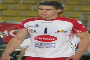 Ein Mann in rot-weißer Handballdress steht auf einem Feld, umgeben von Zuschauern, mit einem roten Banner im Hintergrund, auf dem "Krasnoyarsk vs Bydgoszcz" steht.