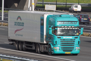 Blauer Sattelschlepper auf einer Autobahn neben einer Brücke mit Geländern, Pfählen, Brettern und Gras, mit anderen Fahrzeugen auf der Straße zu sehen.