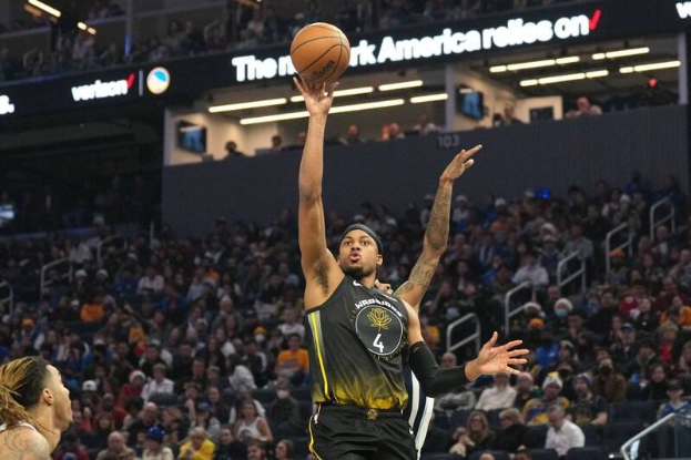 Ein Basketballspieler in einem schwarzen und gelben "Golden State Warriors"-Trikot wirft den Ball in einem hell erleuchteten Stadion voller Zuschauer.