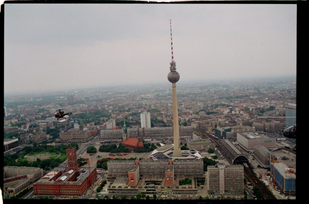 Luftaufnahme von Berlin, Deutschland, mit dem Fernsehturm in der Mitte, umgeben von Gebäuden, Bäumen, Straßen, Fahrzeugen und einem Hubschrauber.