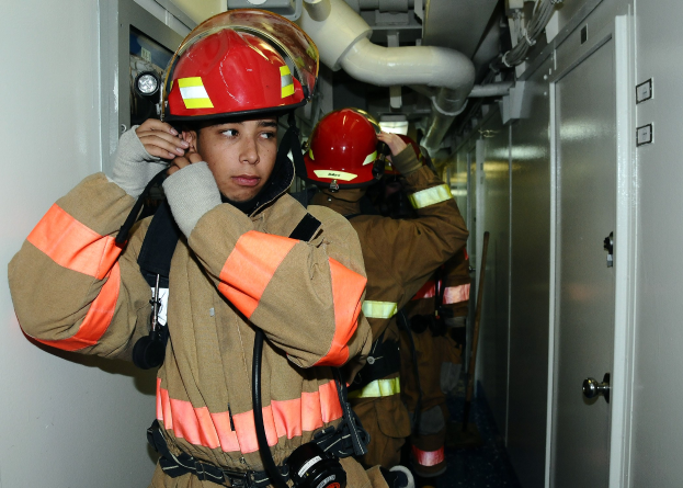 Feuerwehrleute in Uniform während eines Übungseinsatzes in einem Raum stehend, mit Rohren und Gegenständen im Hintergrund.