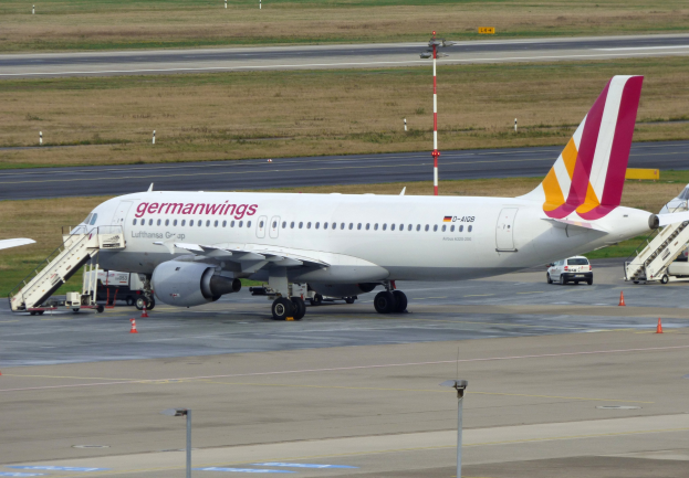 Germanwings Airbus A320-200 geparkt am Frankfurter Flughafen mit Bodenfahrzeugen, Verkehrskegeln, Versorgungsmasten und Grünfläche im Hintergrund.