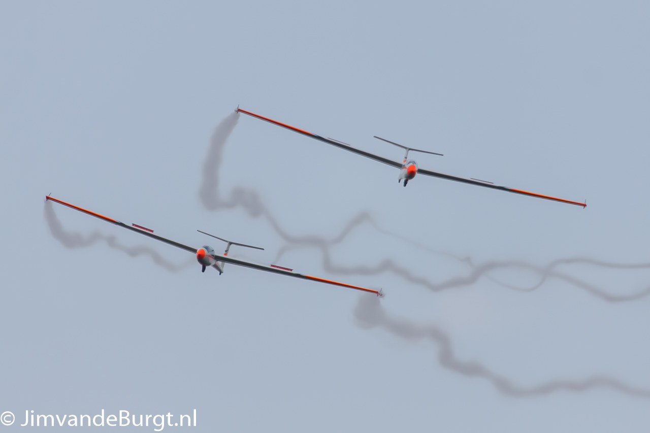 Zwei Segelflugzeuge am Himmel mit Rauchspuren, mit Text in der unteren linken Ecke.