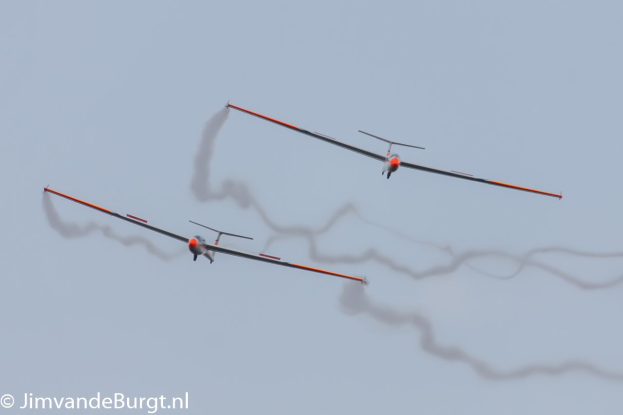 Zwei Segelflugzeuge am Himmel mit Rauchspuren, mit Text in der unteren linken Ecke.