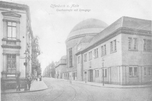 Ein altes Schwarz-Weiß-Foto einer Stadtstraße namens Goethestraße in Offenbach am Main, das Gebäude, Straßenlaternen, Straßenlaternen, Bäume und Menschen auf der Straße zeigt, mit der Aufschrift "Offenbach a Main, Goethestraße mit Synagoge" oben.