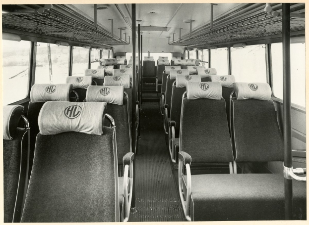 Altes Schwarz-Weiß-Foto eines Businneren mit mehreren Sitzen, Stangen und Glasfenstern, mit Text am unteren Rand.