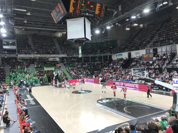 Basketballspiel in großer Arena mit Zuschauern, mit Teams Asvel und Galatasaray, und Anzeigetafel und Beleuchtung oben