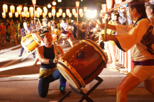 Männer, die auf einem Festival Trommeln spielen, mit Lichtern darüber.