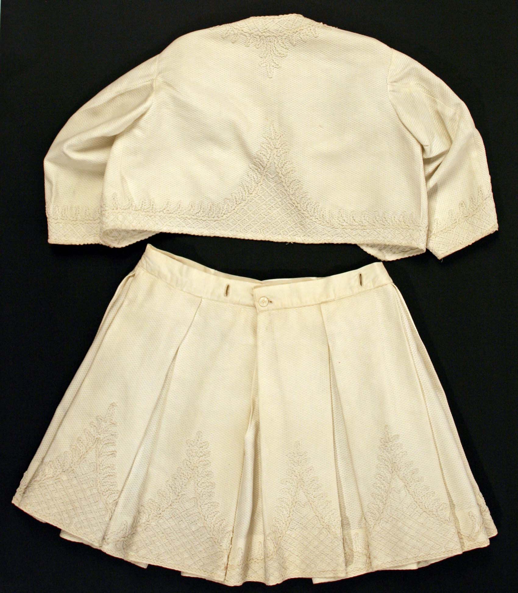 Weiße knielange Plisse-Rock mit hohem Bund und ärmelloser Rundhalspullover auf schwarzem Hintergrund, beide aus leichtem Stoff mit feiner Schimmer.