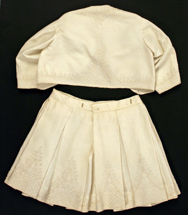 Weiße knielange Plisse-Rock mit hohem Bund und ärmelloser Rundhalspullover auf schwarzem Hintergrund, beide aus leichtem Stoff mit feiner Schimmer.