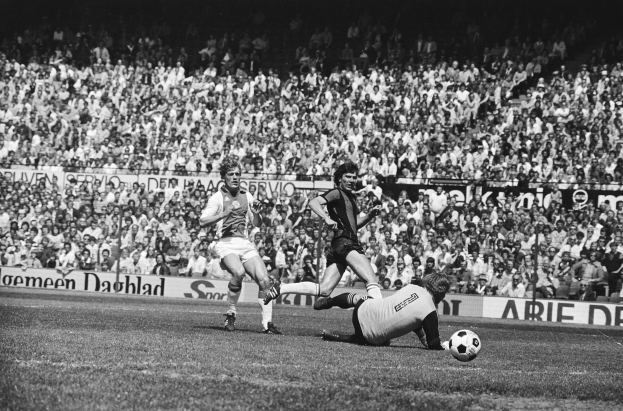 Schwarzes Foto von Männern, die Fussball spielen, auf einem Feld mit Zuschauern im Hintergrund und einer Bundesliga 1978-79 Ajax 1-1 Hannover 96 Fahne.